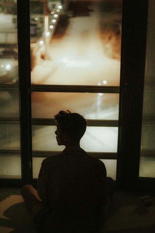 Free Artistic silhouette of a person sitting by a window at night, capturing a moody and introspective atmosphere. Stock Photo