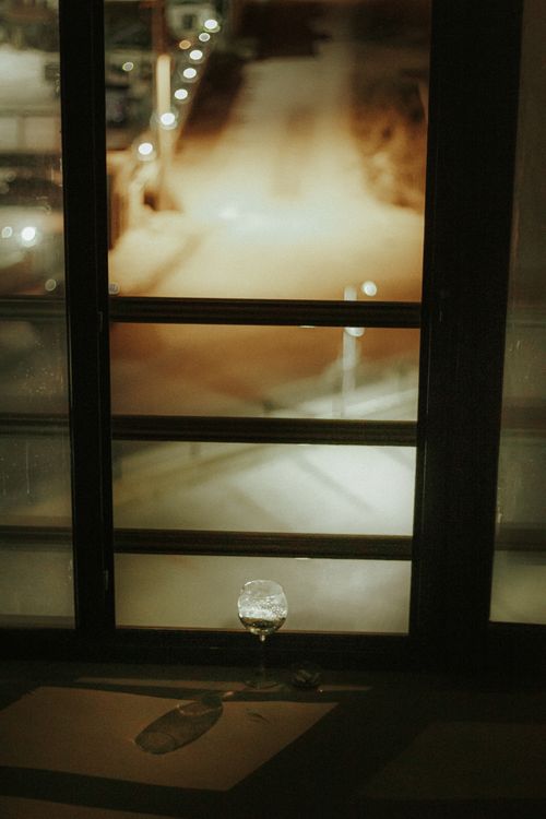 Free A moody night view through a window overlooking a quiet street with muted urban lights. Stock Photo