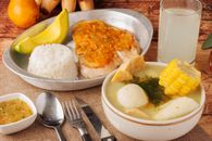 Delight in a traditional Colombian meal featuring ajiaco soup, rice, avocado, and tamarind juice.