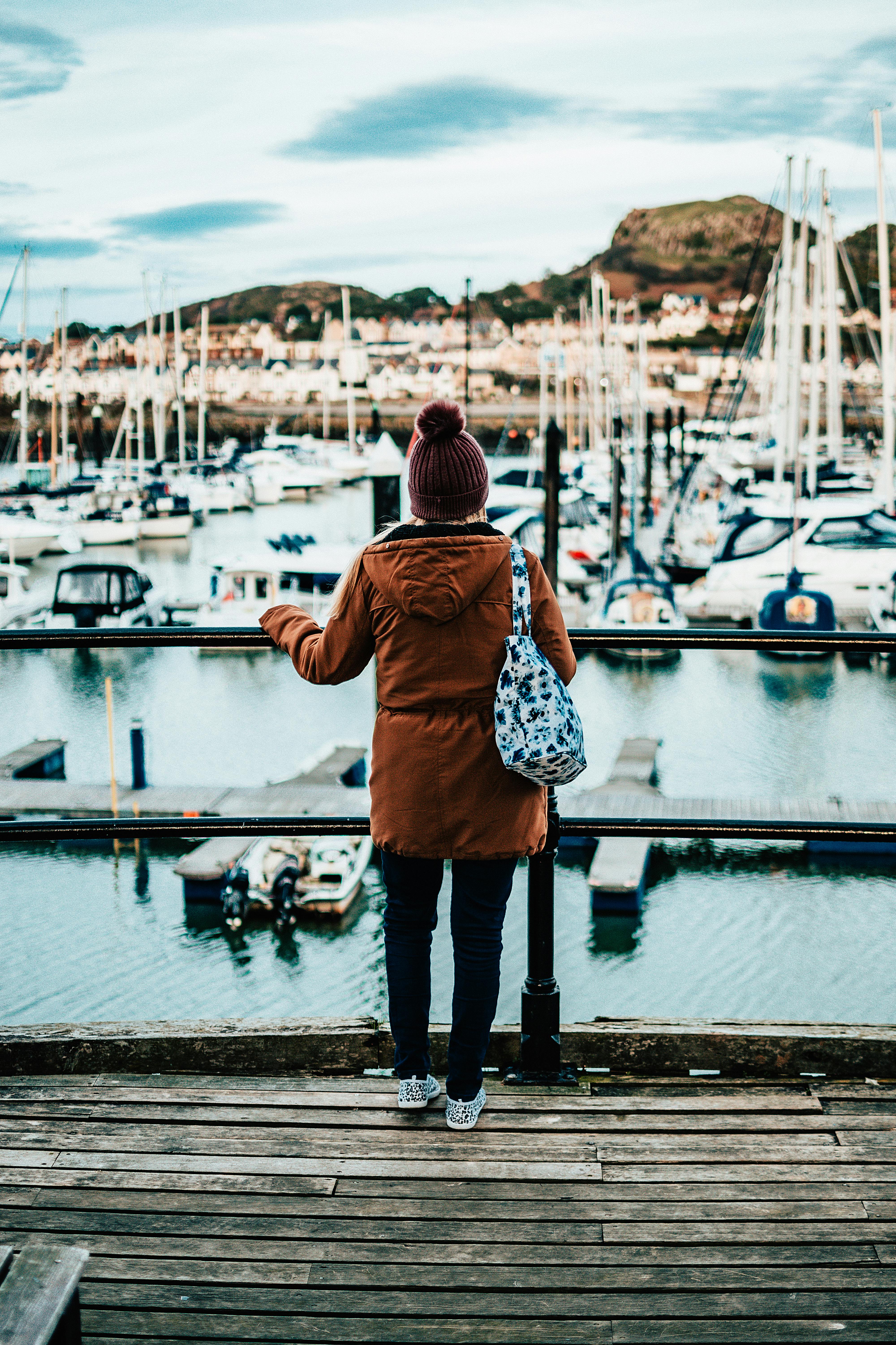 一名妇女站在木制码头上，俯瞰威尔士一个风景优美、停满船只的码头