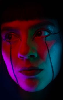 Close-up portrait of a person with vibrant neon lighting and artistic makeup.
