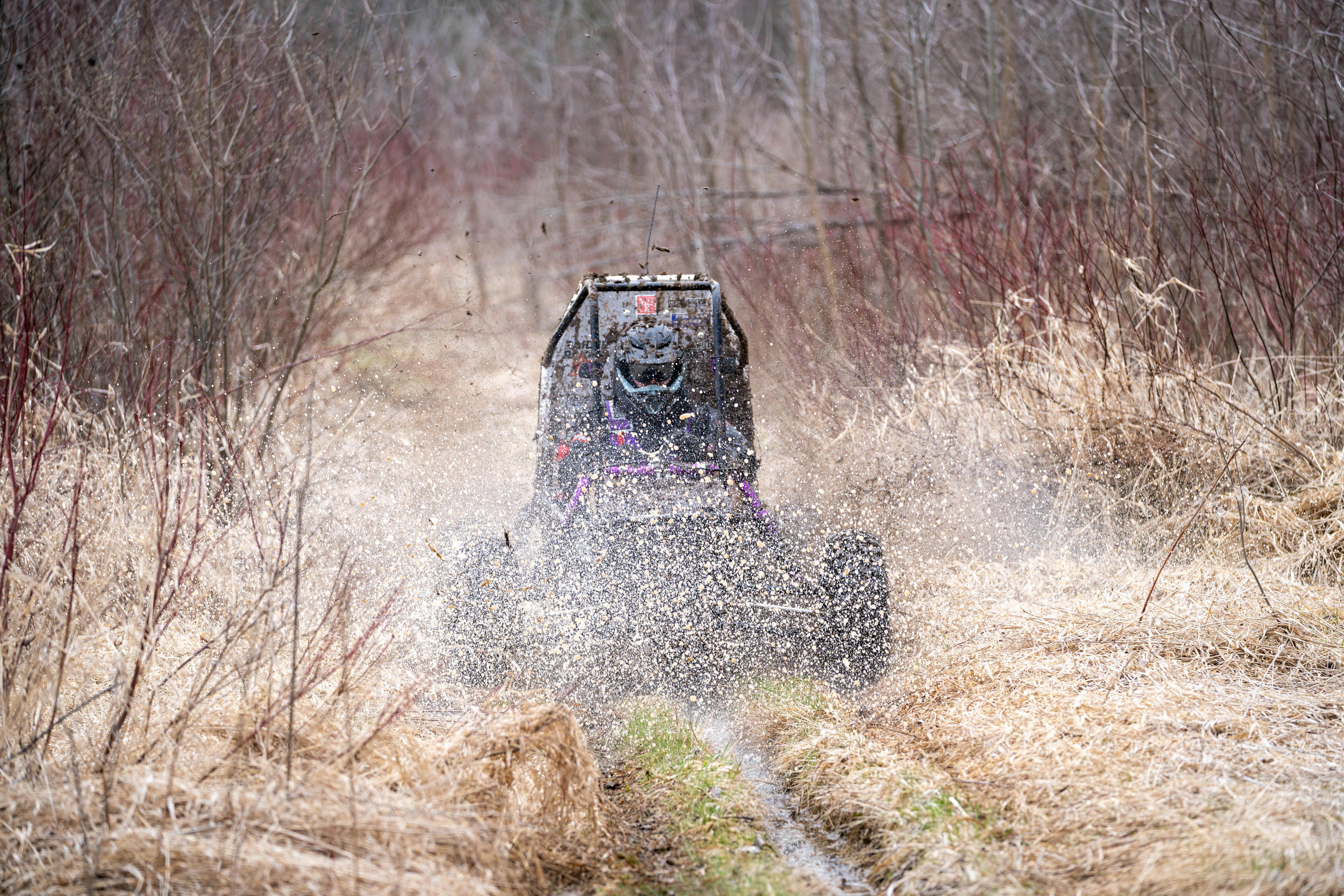 All-terrain vehicle splashing through mud on a forest trail during an adventure ride.