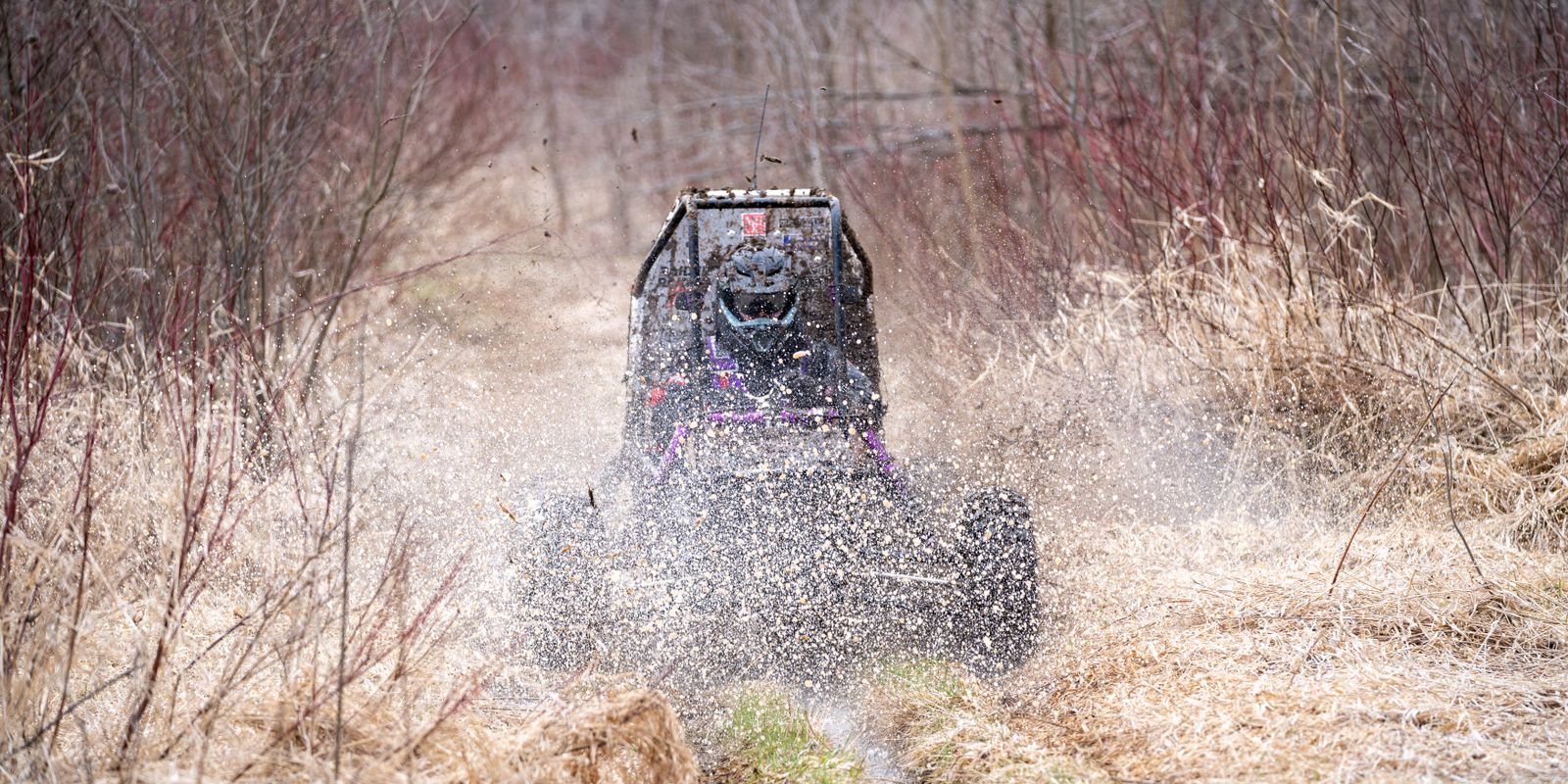 An all-terrain vehicle splashing through mud on a forest trail
