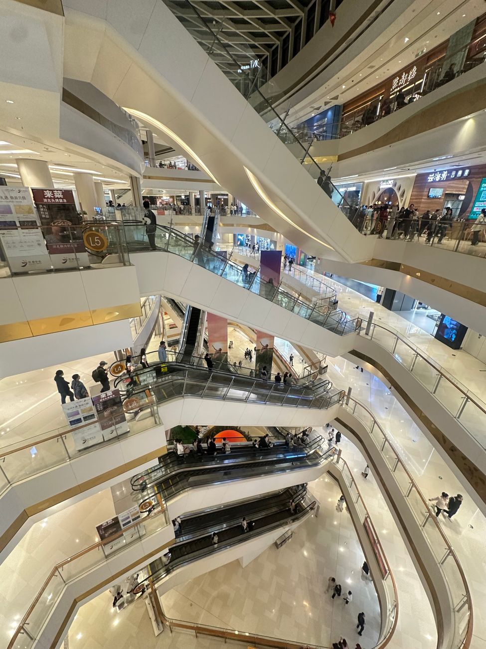 A multi-level view of a bustling shopping mall in Suzhou with escalators and bright lighting.