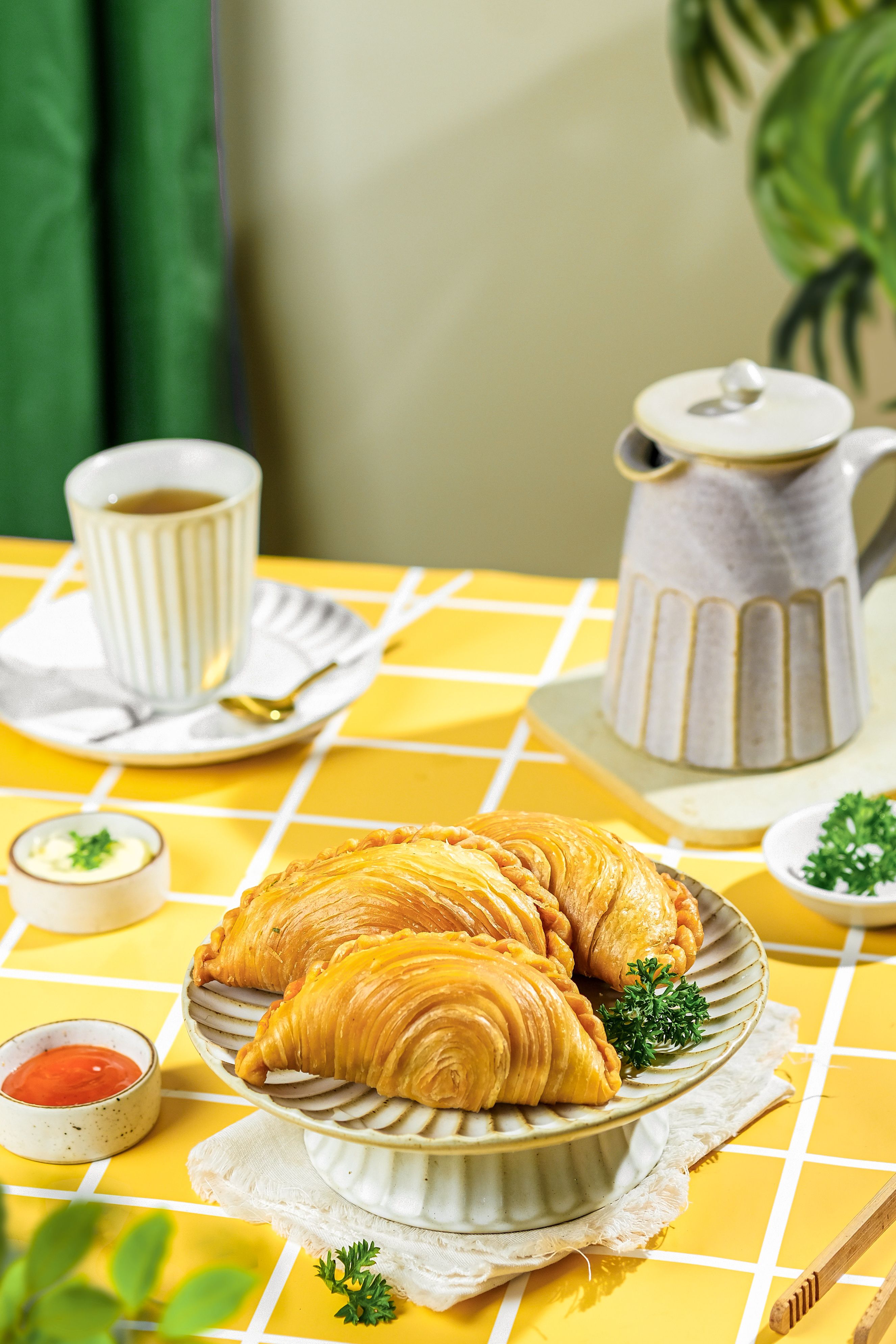 Gratuit De délicieux beignets de curry indonésiens servis sur une table à motifs avec du thé, créant une ambiance chaleureuse et conviviale. Photos