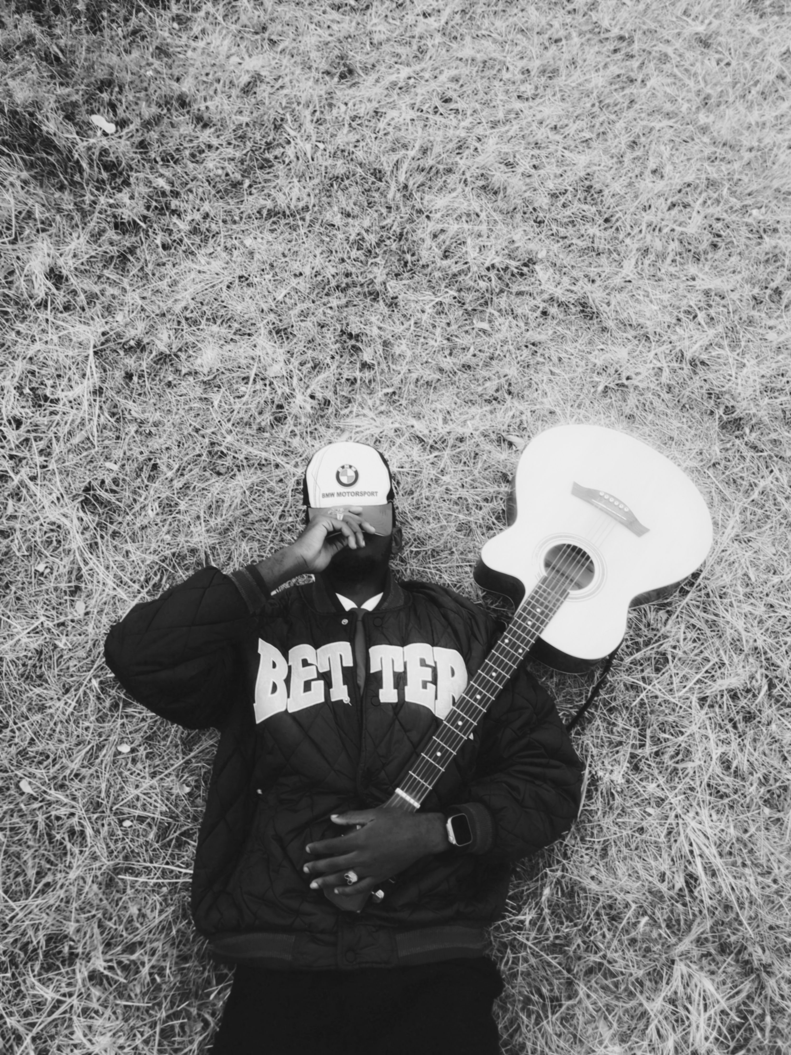Black and white photo of a man lying on grass with a guitar, capturing a serene moment.