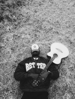 A person lies on grass holding a guitar, evoking a casual, artistic vibe.