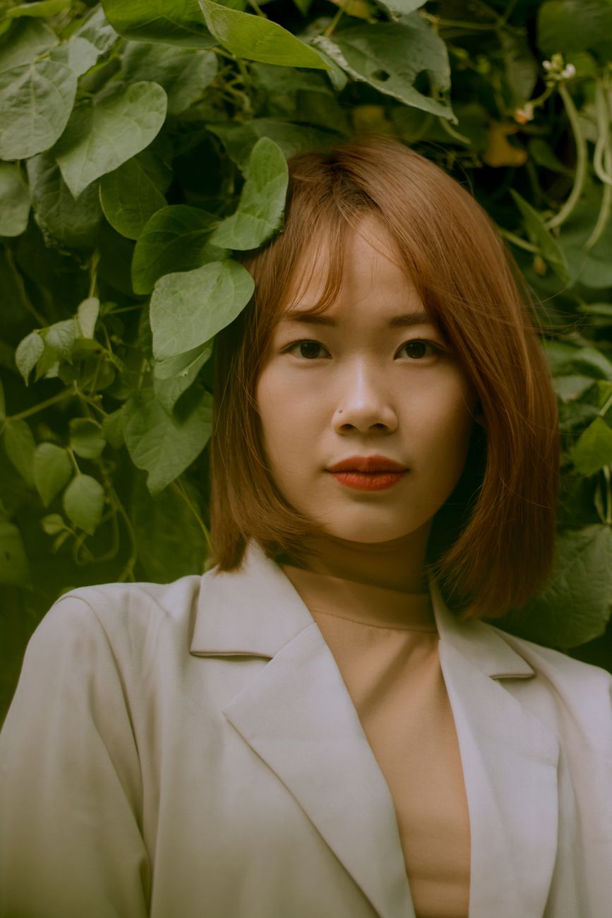 Elegant portrait of an Asian woman surrounded by lush green leaves outdoors in Qinghai, China.