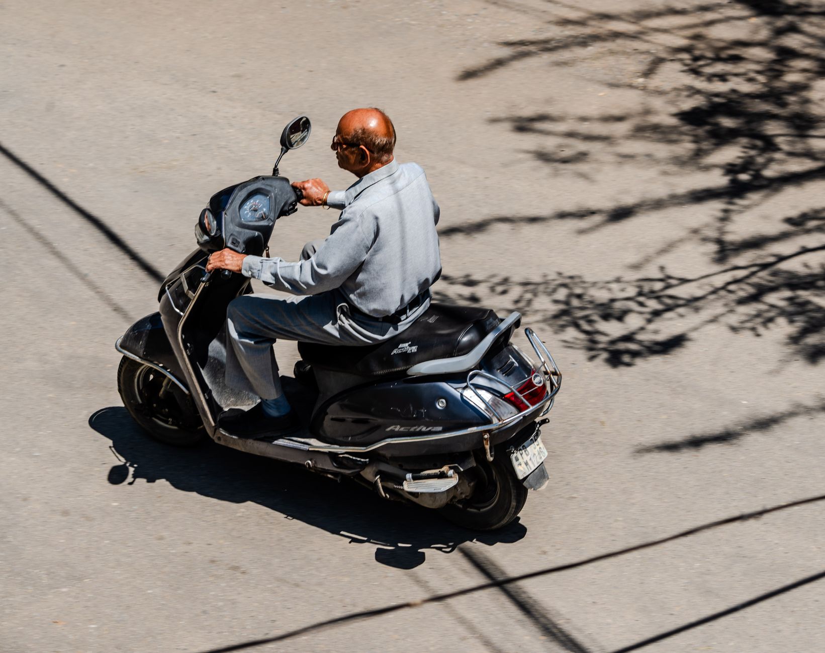 A senior man riding a scooter on a sunny day, seen from above, capturing motion and urban lifestyle.