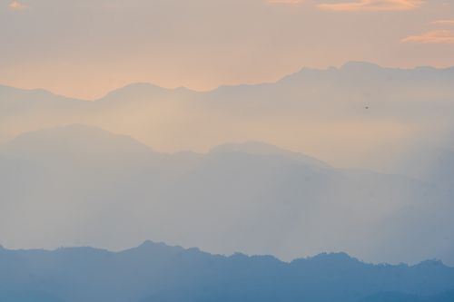 Free A tranquil view of misty mountains during sunrise, showcasing layers of hills with a soft pastel glow. Stock Photo