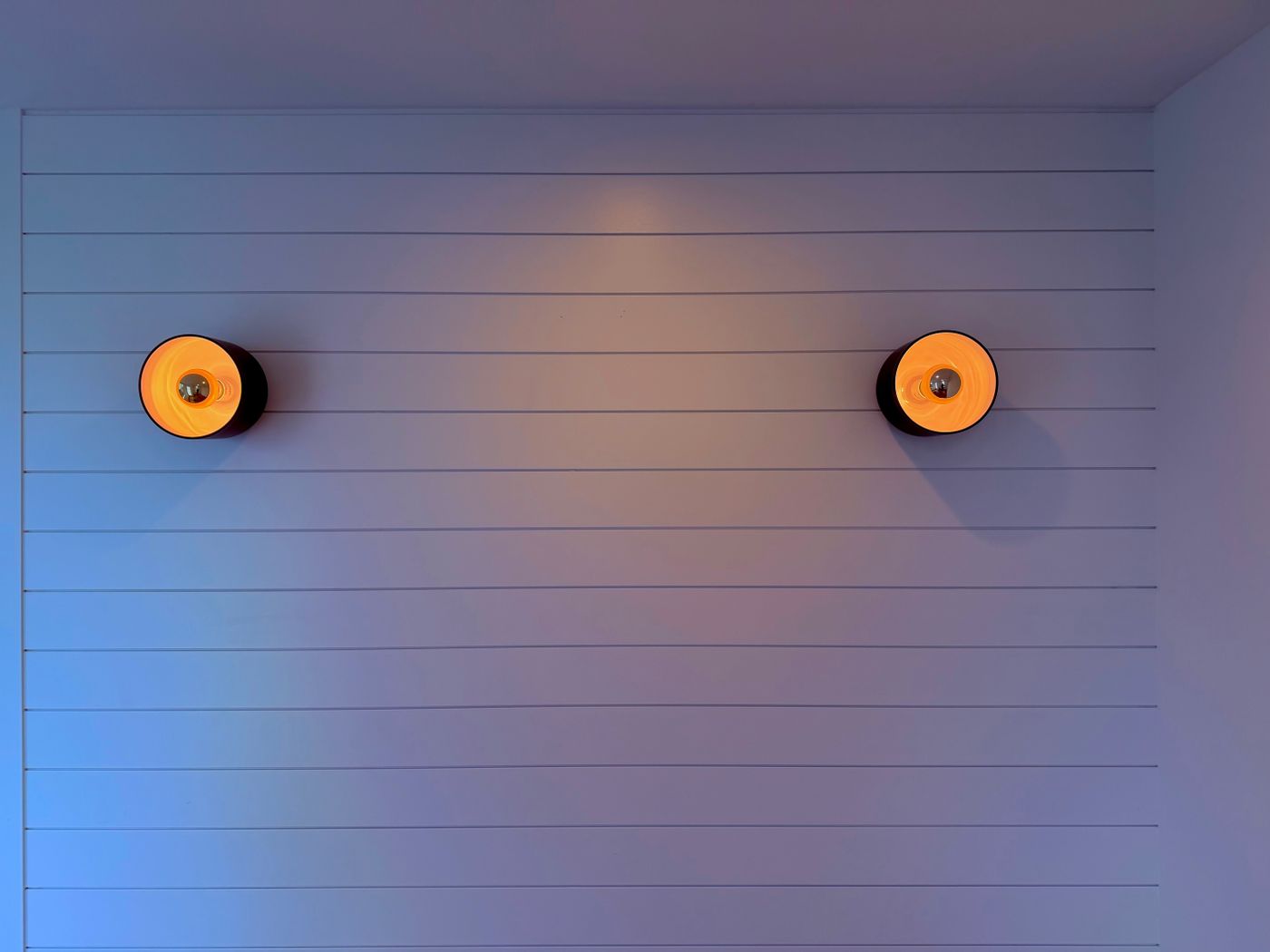 Deux appliques murales allumées sur un mur à panneaux dans un intérieur contemporain