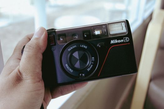 Close-up of a vintage Nikon camera held by a hand, capturing nostalgia of film photography.