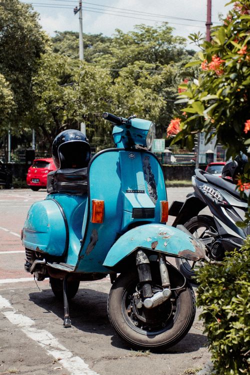 Free A classic blue scooter parked outdoors surrounded by greenery, exuding a vintage vibe. Stock Photo