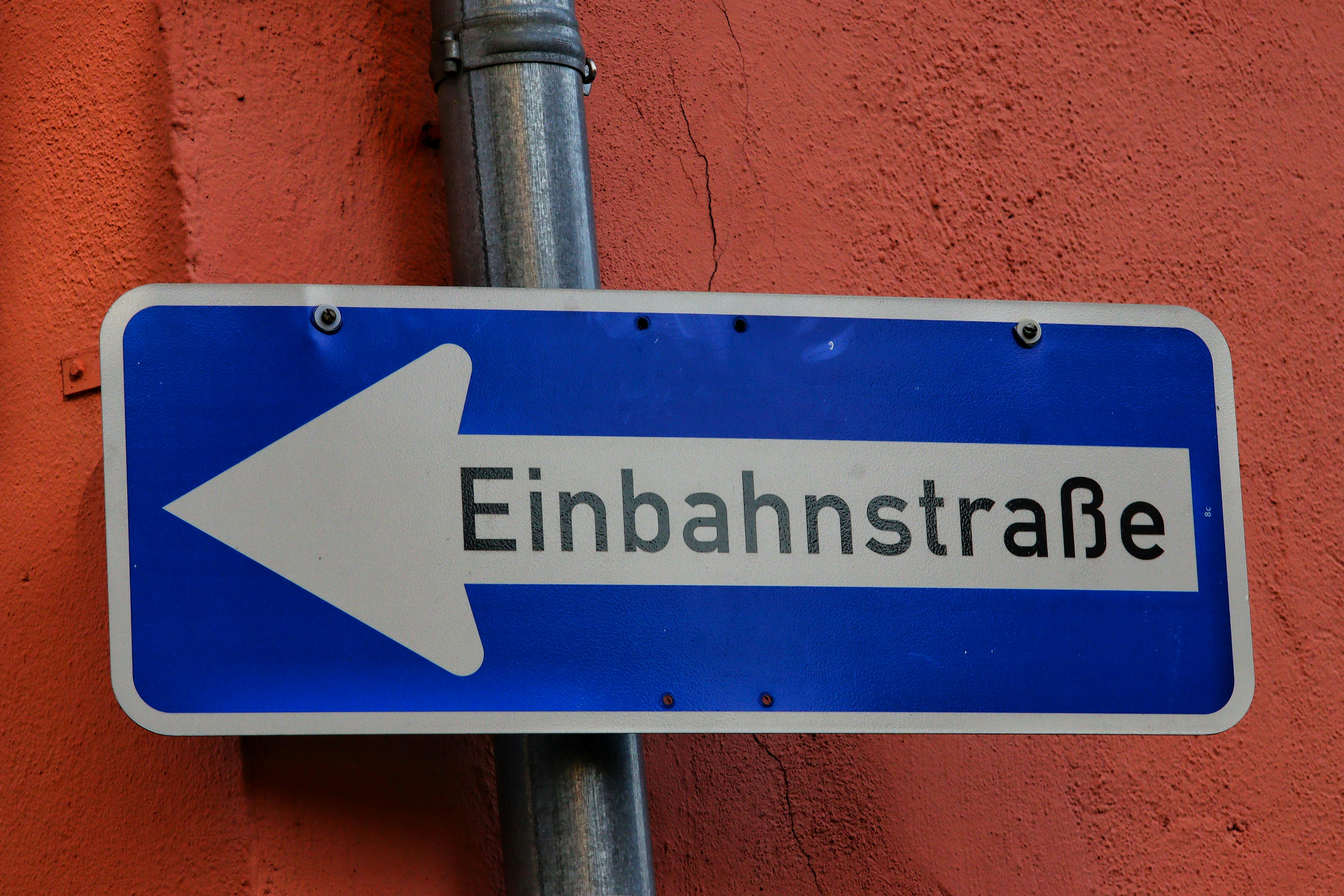 Blue one-way street sign with arrow labeled 'Einbahnstraße' against an orange wall.