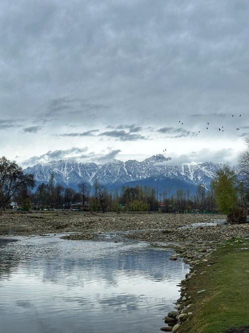 Free Tranquil scene of mountains and river reflecting snowy peaks and cloudy skies. Stock Photo
