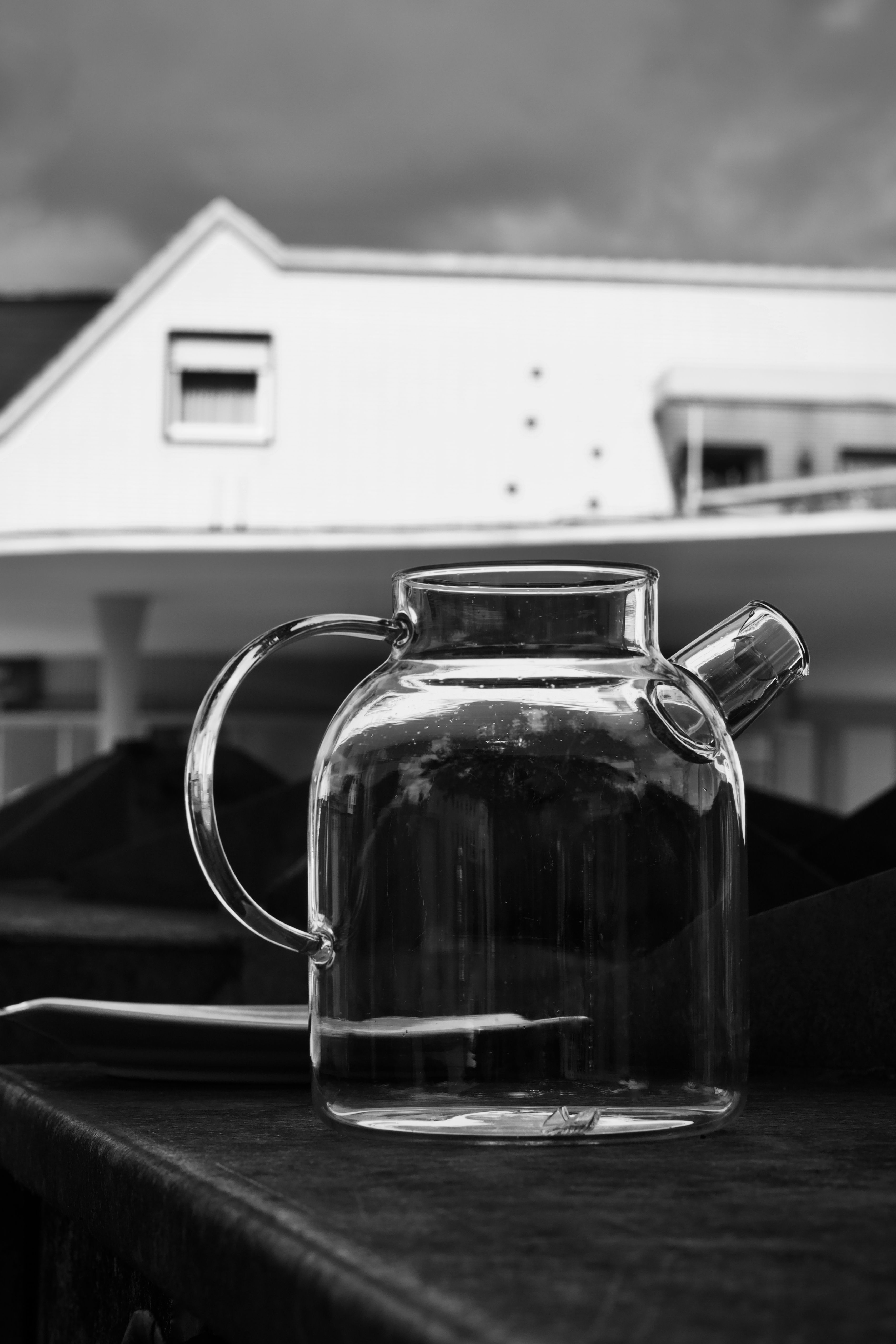 A clear glass teapot against a modern urban building in black and white.
