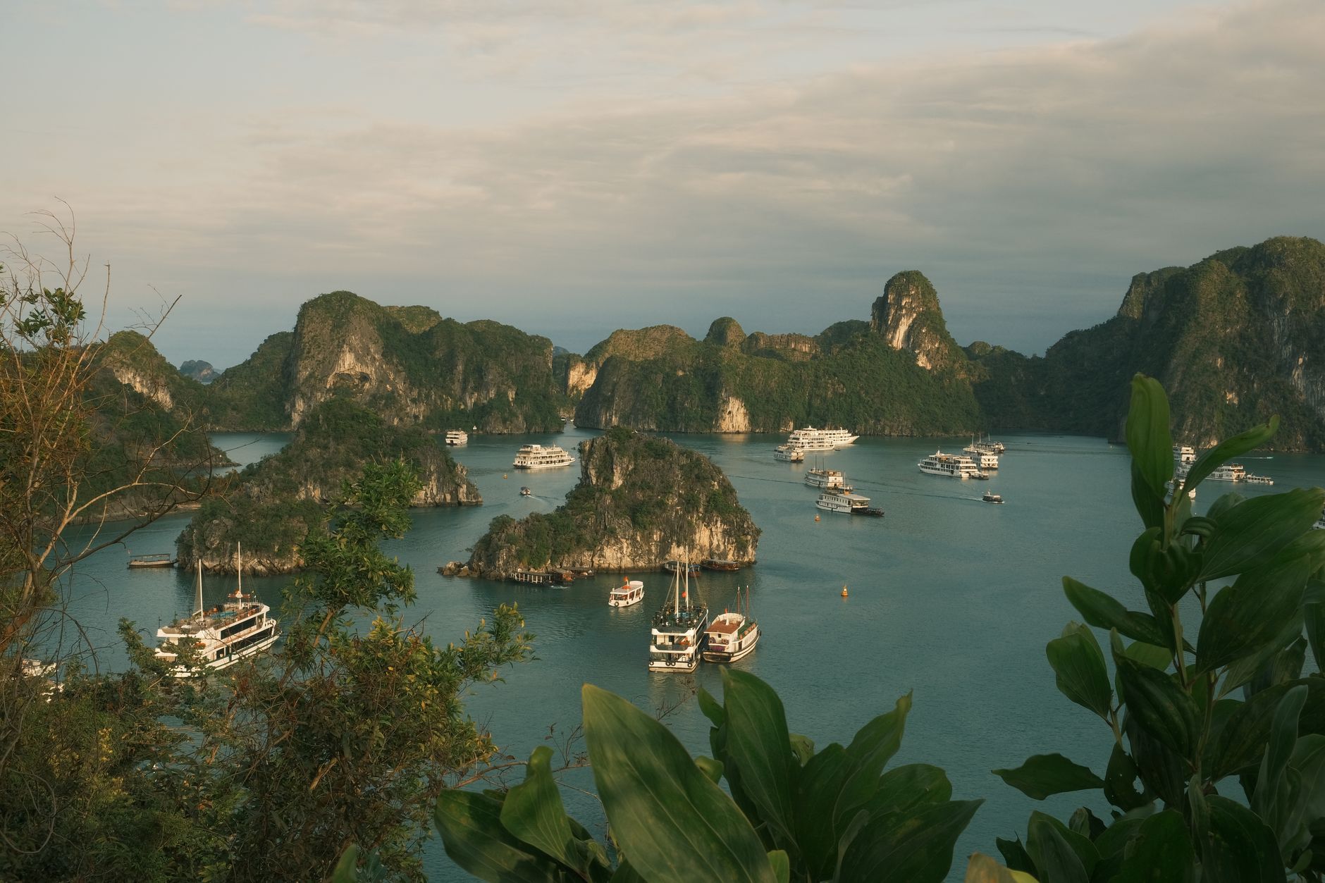 Scenic view of Halong Bay with boats and limestone islands under a cloudy sky.
