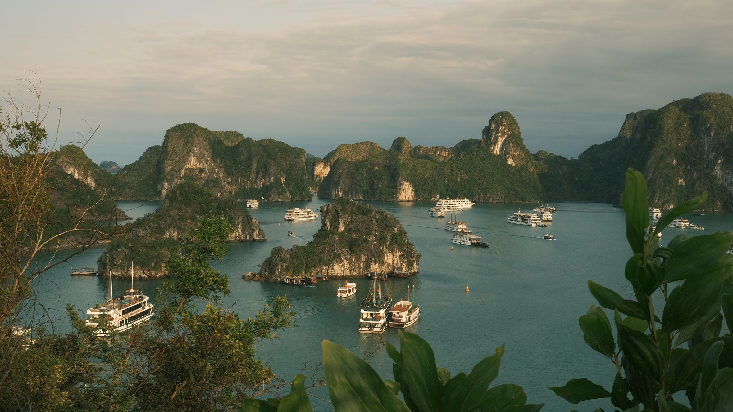 Scenic view of Halong Bay with boats and limestone islands under a cloudy sky.