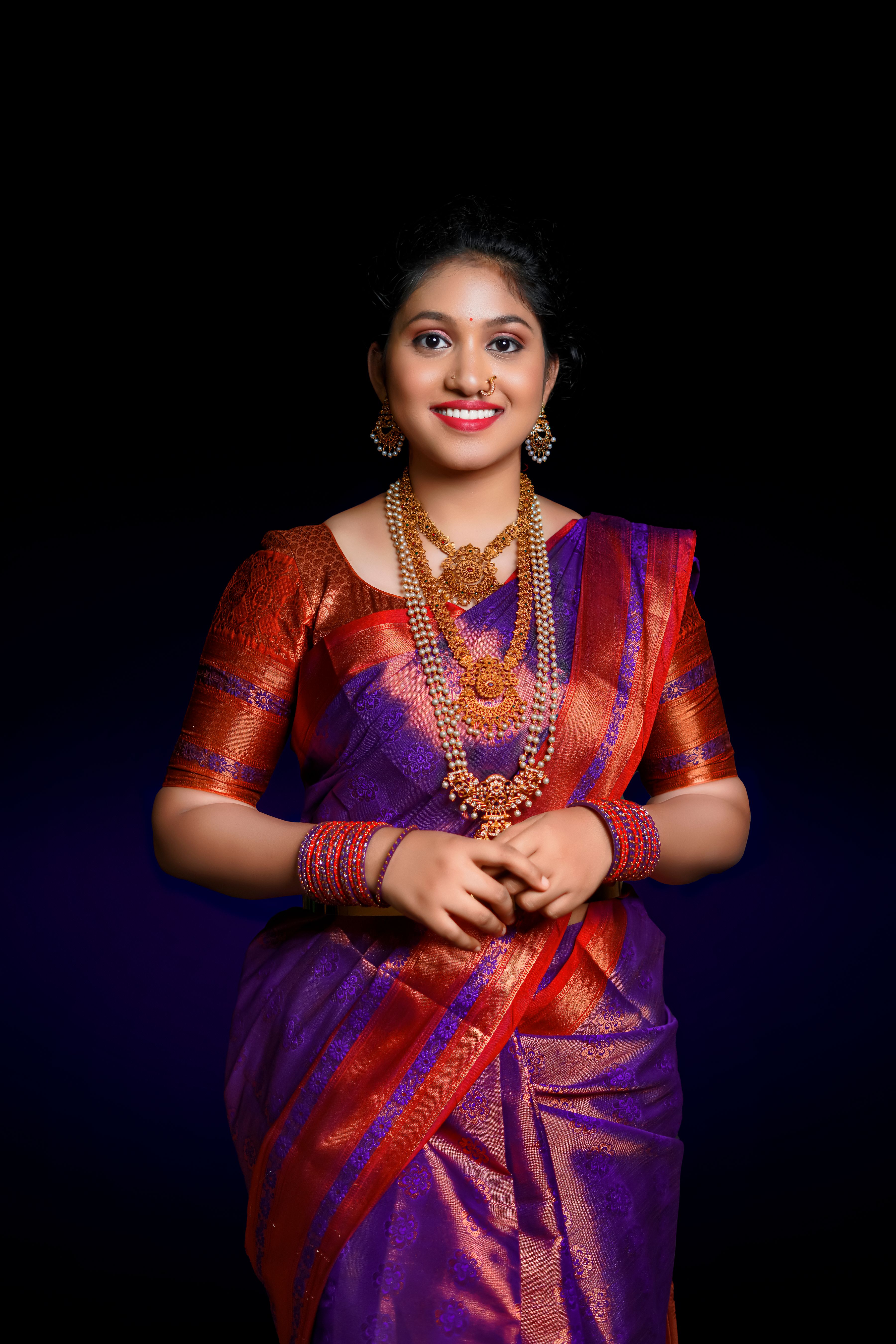 Portrait of a smiling woman wearing a traditional purple and red sari with gold jewelry.