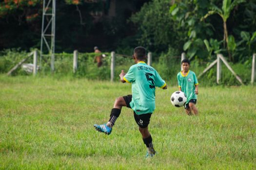 Teenagers play soccer on a lush field in Myawaddy, Myanmar, showcasing sports and teamwork.