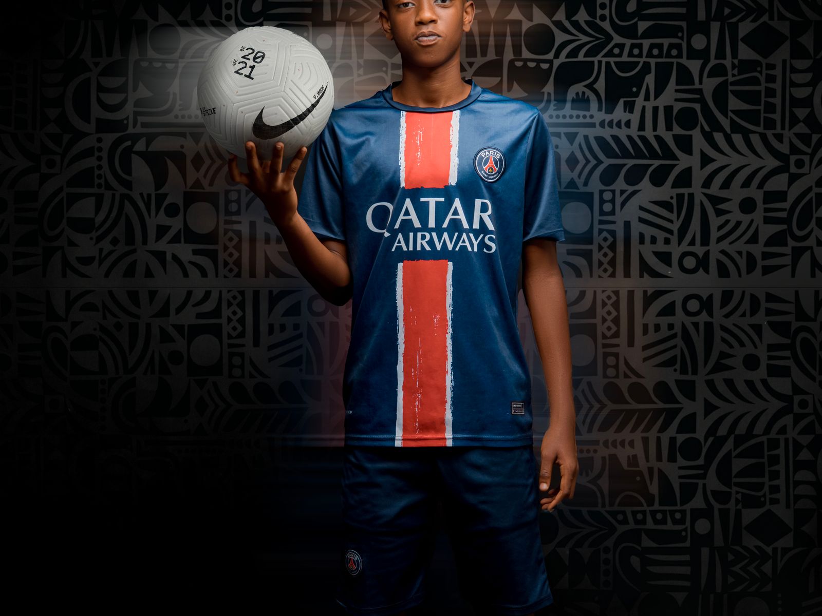 Young player in a blue jersey holding a football in a studio