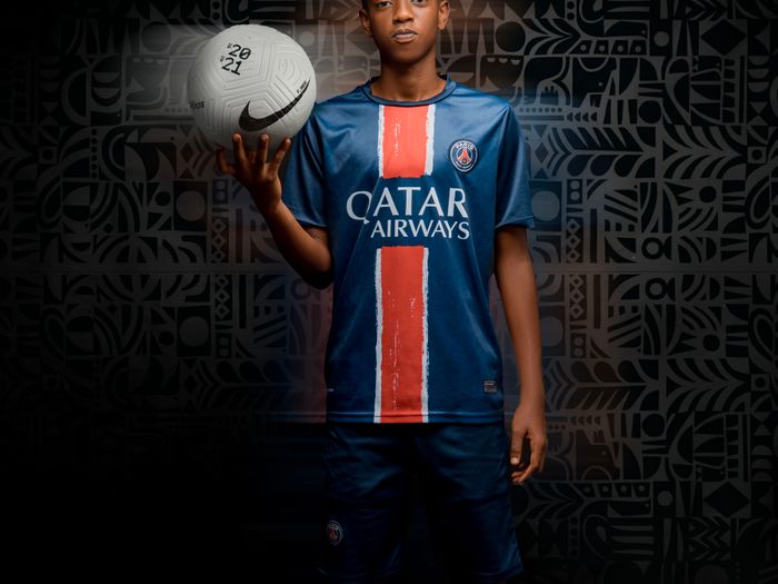 Young player in a blue jersey holding a football in a studio