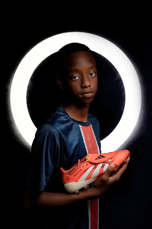 Free Portrait of a young soccer player holding orange cleats under a studio light ring. Stock Photo