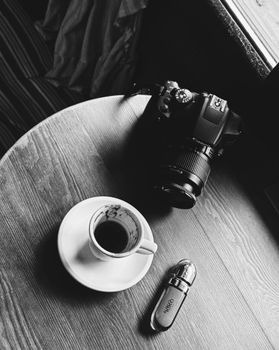 Monochrome image of a camera, coffee cup, and USB drive on a wooden table.