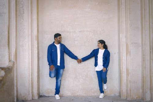 Free A happy couple in matching blue denim standing and holding hands against a textured wall. Stock Photo