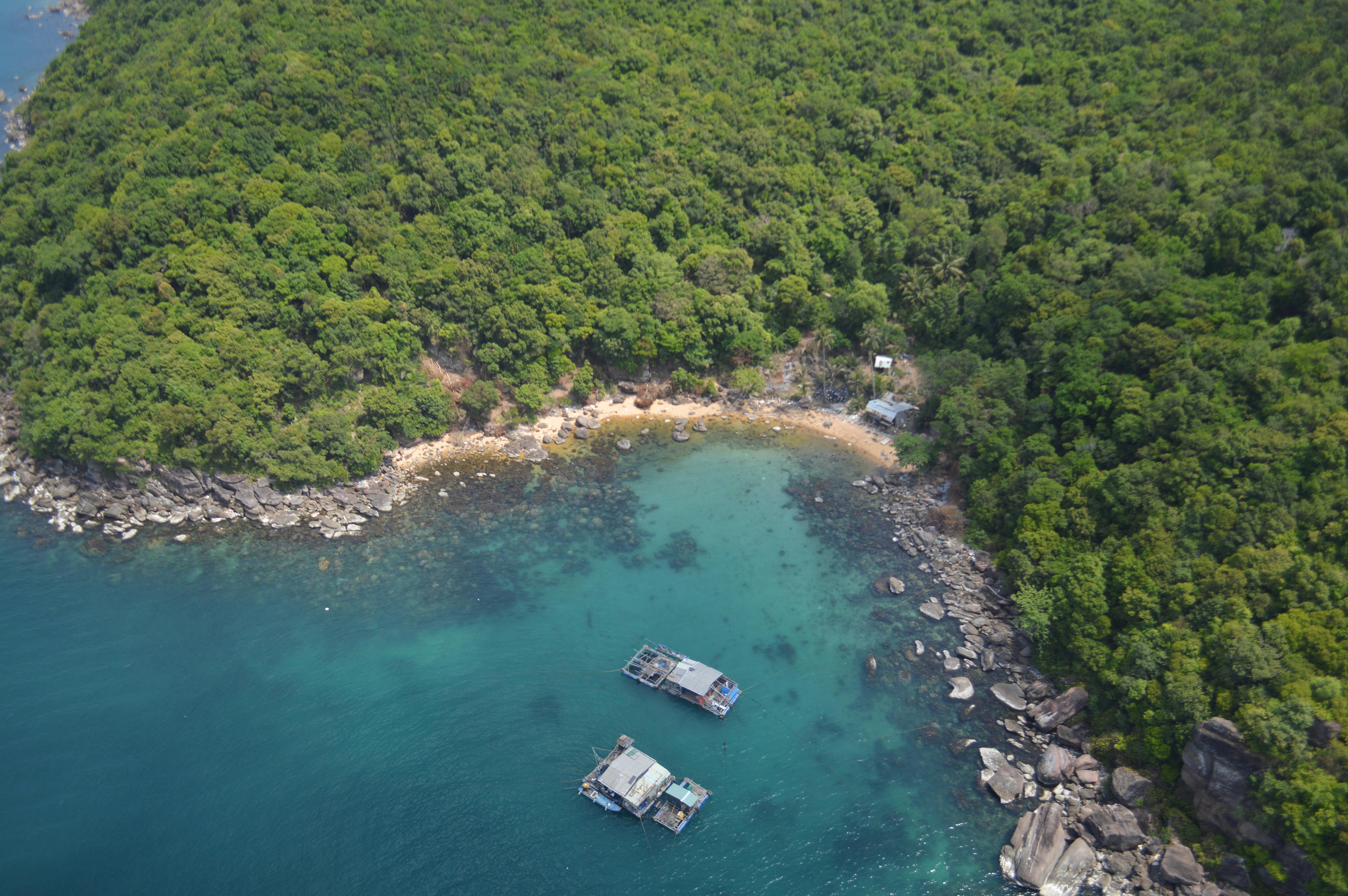 Aerial view of a secluded tropical coastline with lush forests, clear blue water, and floating houses.