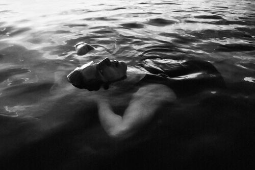 Free Artistic black and white photo of a man floating in water showing serene expression and reflection. Stock Photo
