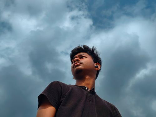 Free A young man gazes upwards with a dramatic cloudy sky backdrop, expressing contemplation and determination. Stock Photo