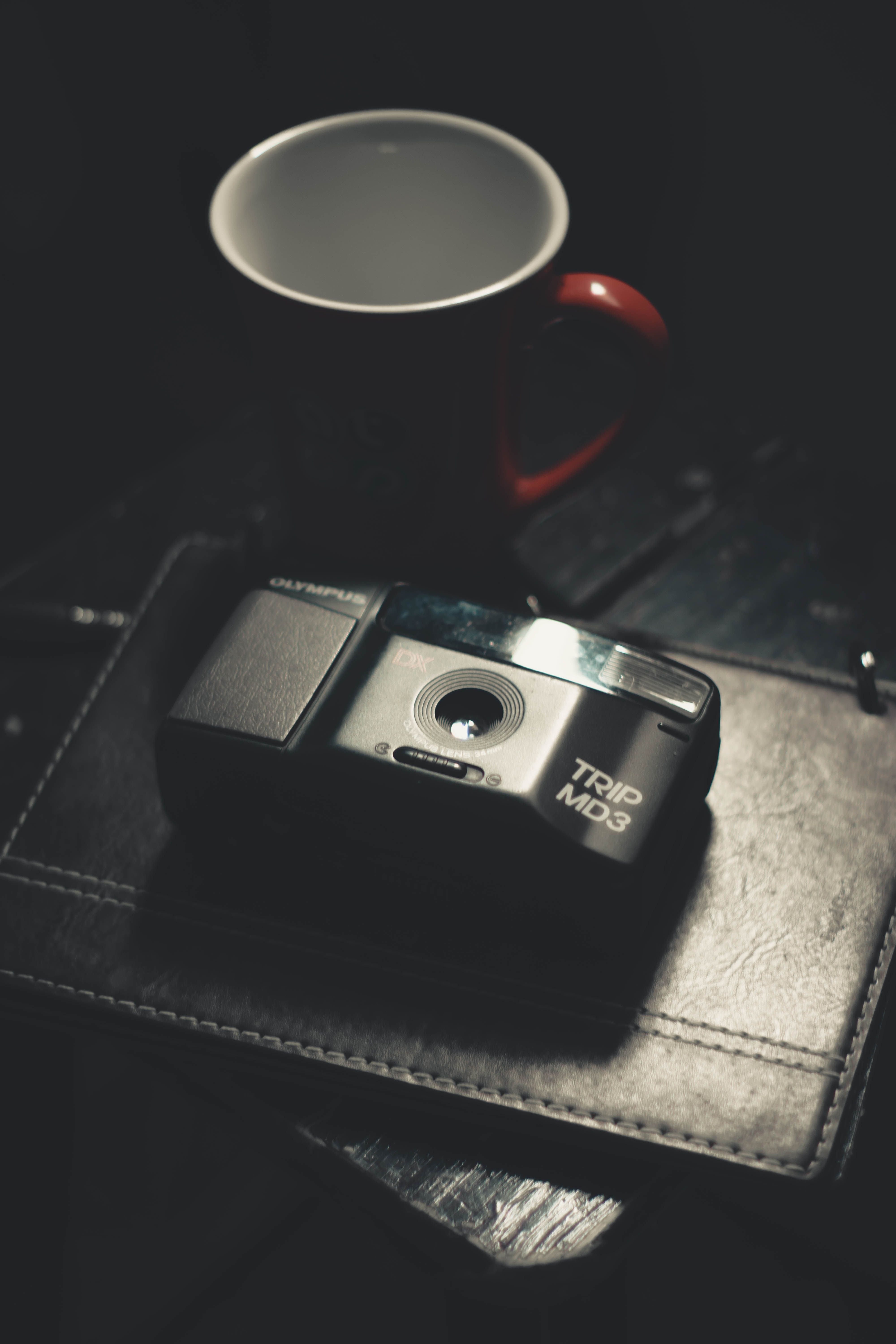 A classic Olympus Trip MD3 camera beside a coffee cup on a leather surface, evoking nostalgia.