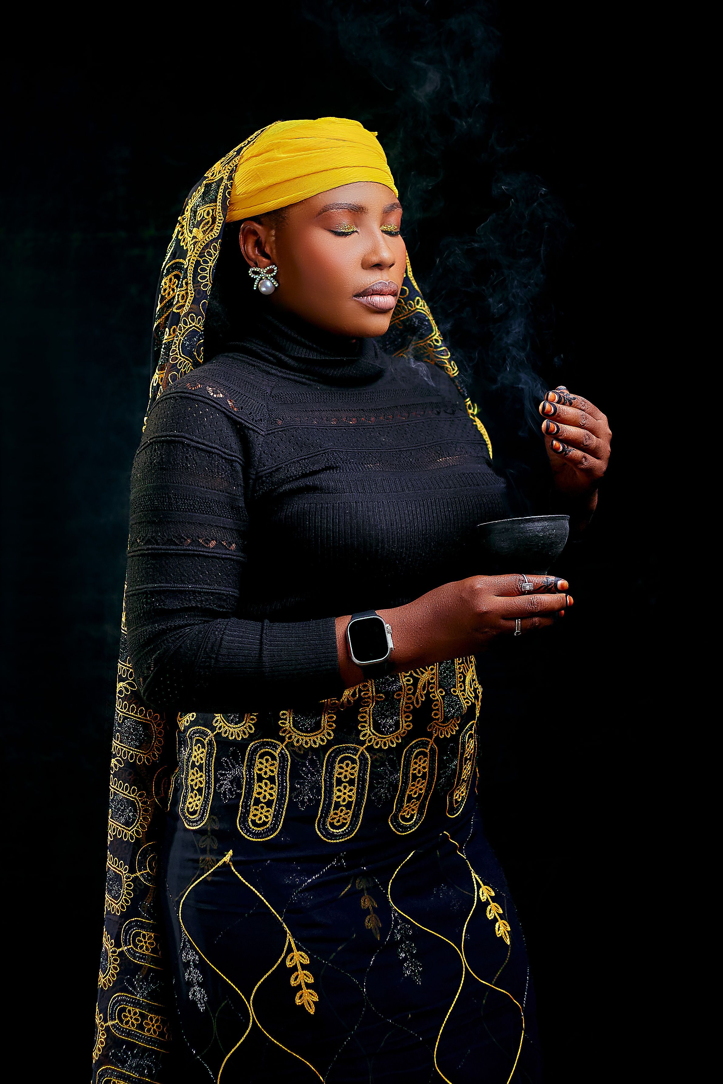 African woman in traditional attire holding a smoking bowl on a black background.