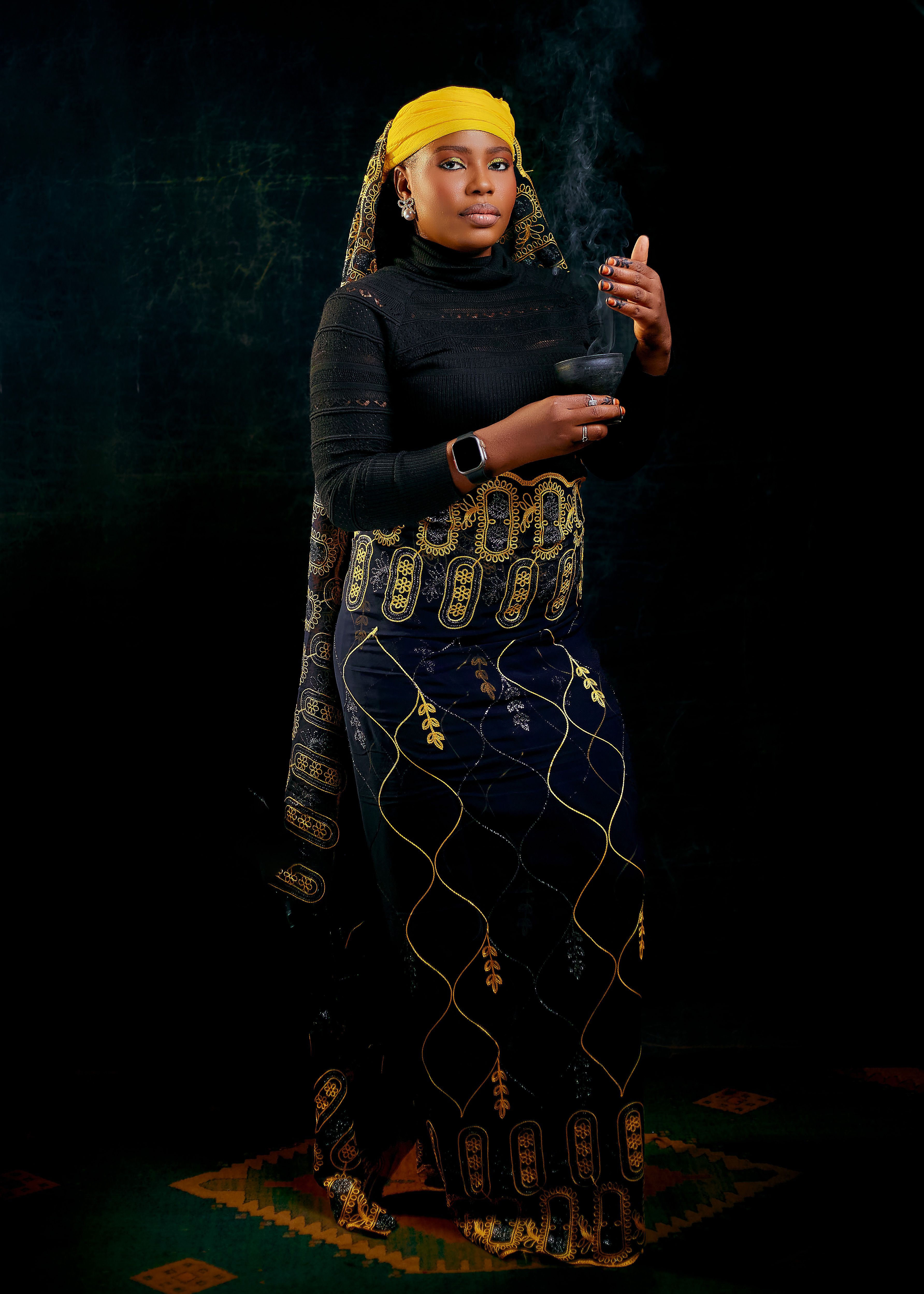 Woman in stylish African fashion holding a bowl against a dark backdrop.