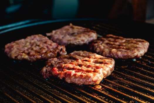 Close-up of four juicy burger patties cooking on an outdoor barbecue grill, perfect for summer grilling.
