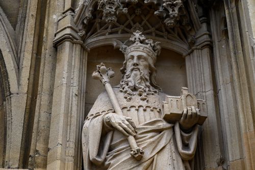 Free Close-up of a detailed stone statue in an English cathedral, depicting a crowned figure holding a model building. Stock Photo