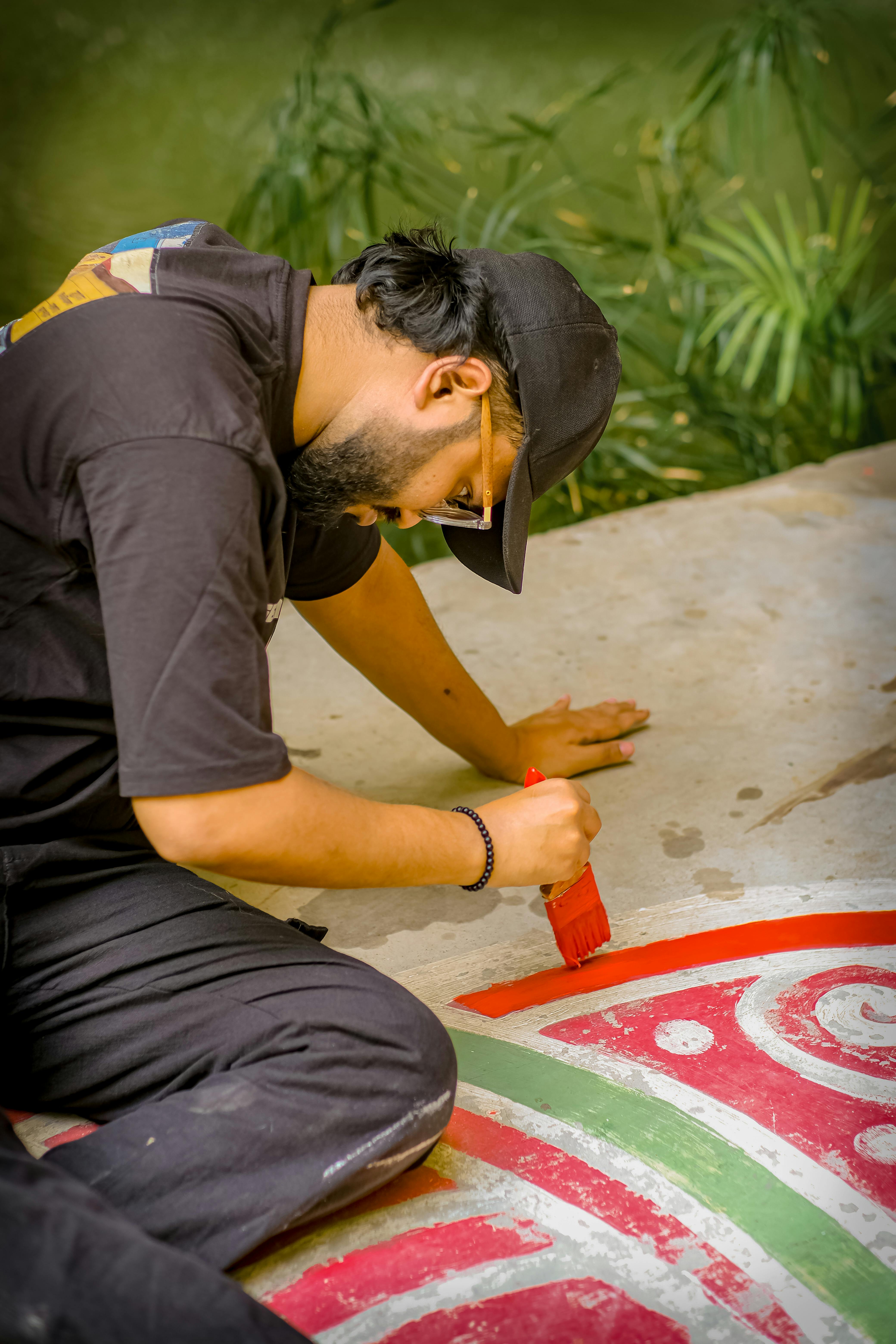 A man painting a vibrant and colorful mural on an outdoor sidewalk with a brush.