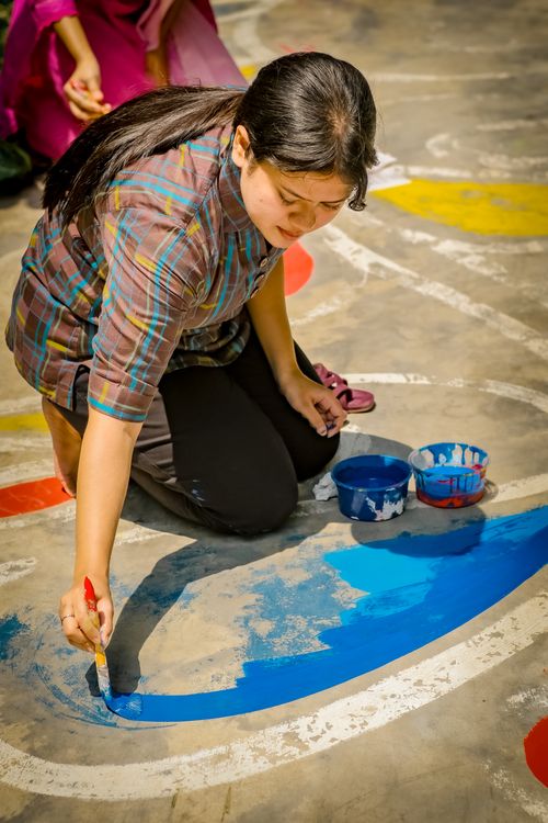 Free A woman focuses on painting a vibrant blue section of a street mural. Stock Photo