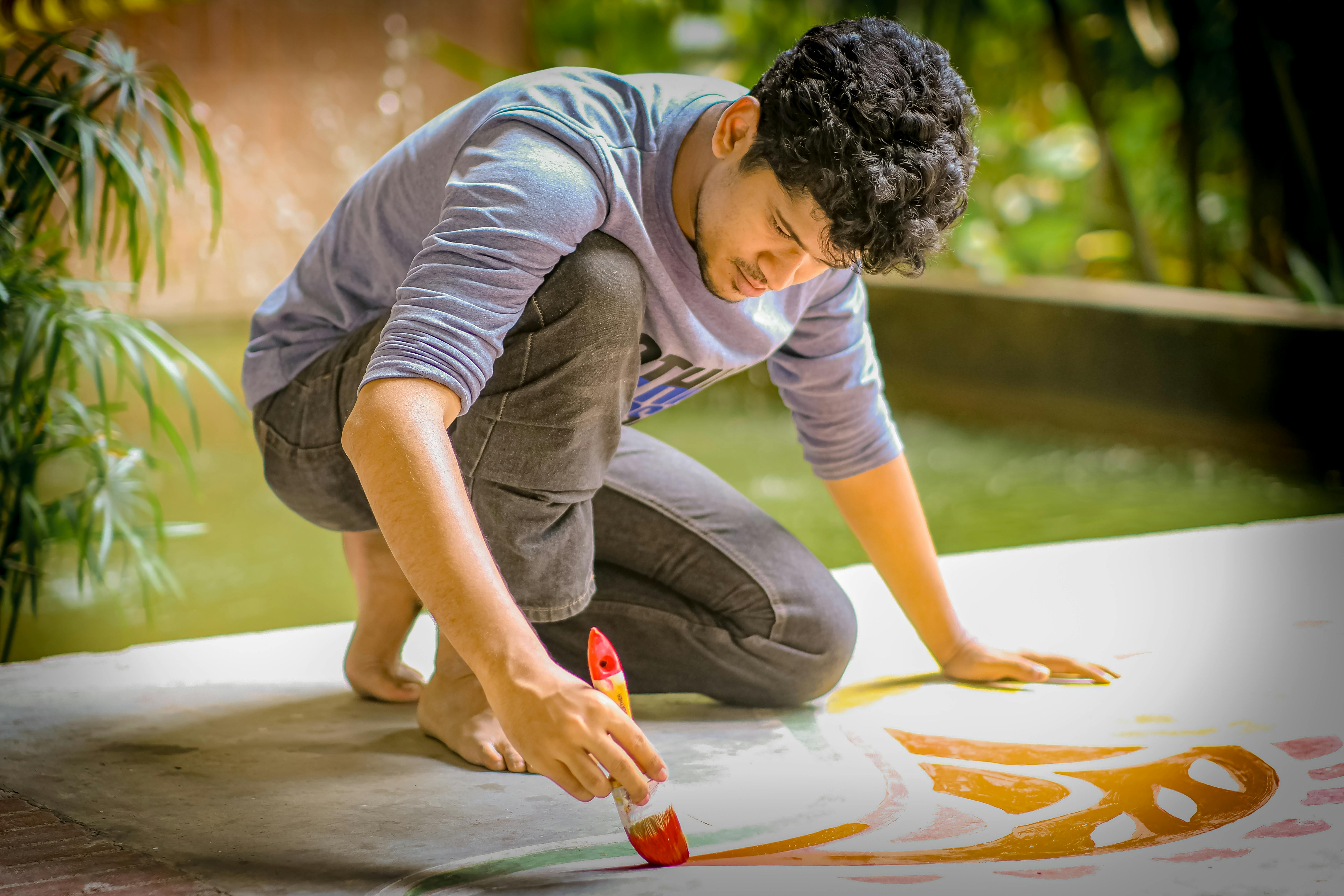 A young man is concentrating on painting a vibrant design outdoors, showcasing his artistic skills.