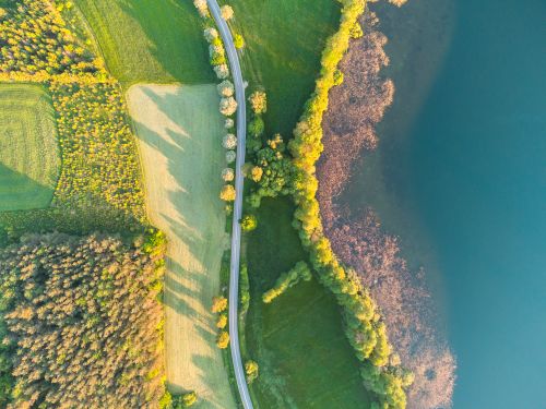 Free A captivating aerial shot of lush green fields, a winding road, and a glistening lake. Stock Photo
