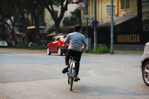 Free A man cycles on an urban street surrounded by vehicles and buildings in broad daylight. Stock Photo