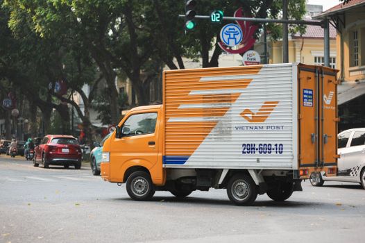Vietnam Post truck navigating a bustling Hanoi intersection on a bright day.