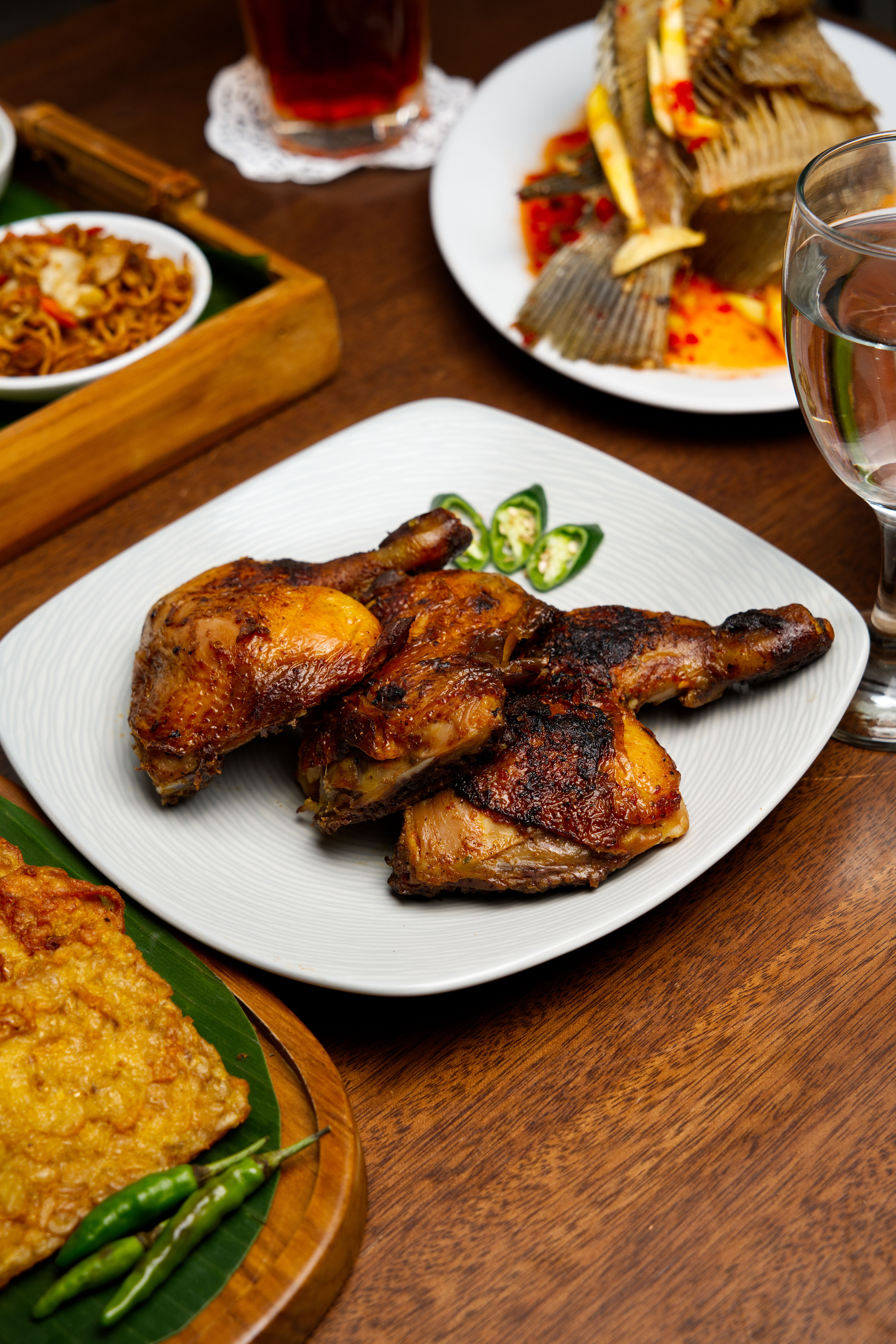 A tantalizing spread of grilled chicken and traditional Indonesian dishes on a wooden table.