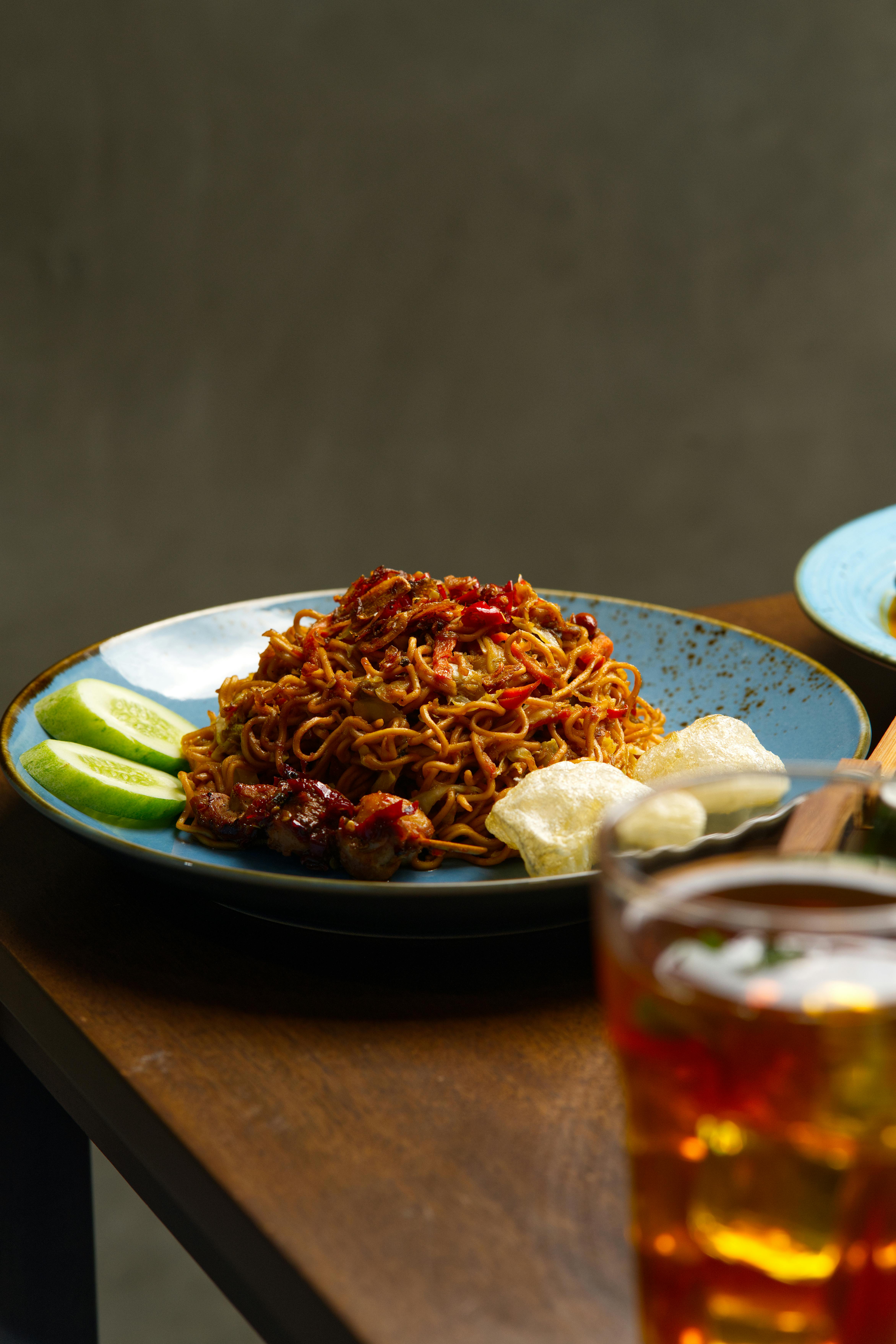Tasty spicy noodles served with lime slices and iced tea on a wooden table.