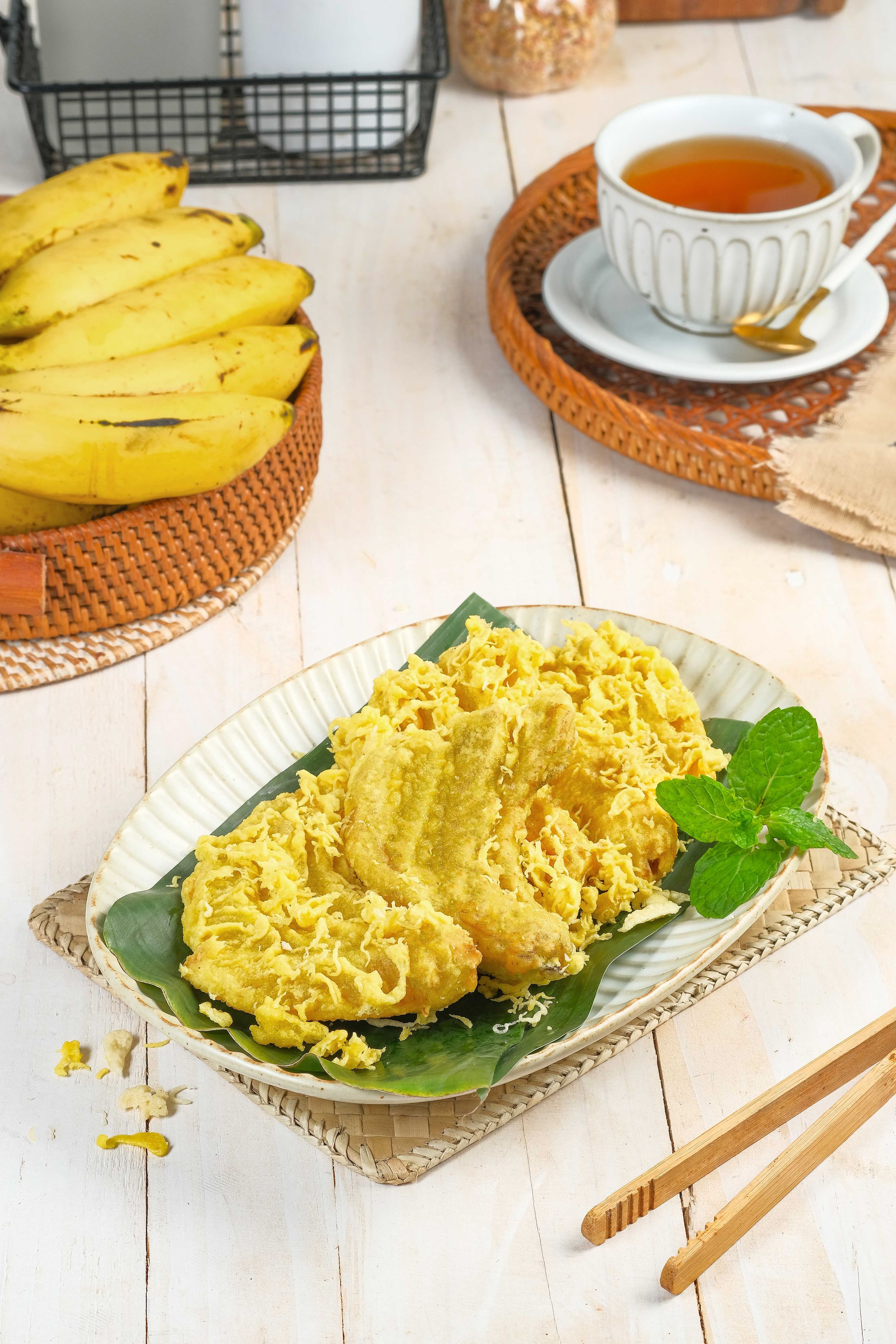Pisang goreng renyah dengan daun mint dan teh di meja kayu