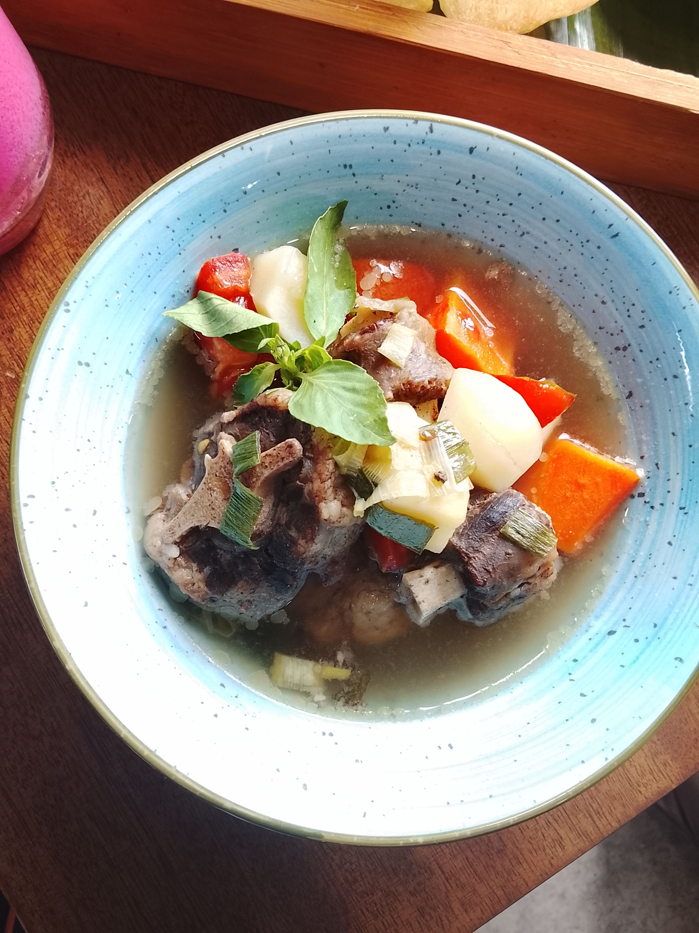Delicious Indonesian oxtail soup with carrots, onions, and fresh herbs in a blue bowl.