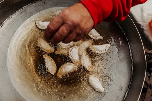 A hand flipping empanadas frying in oil, showcasing traditional Argentine cuisine outdoors.