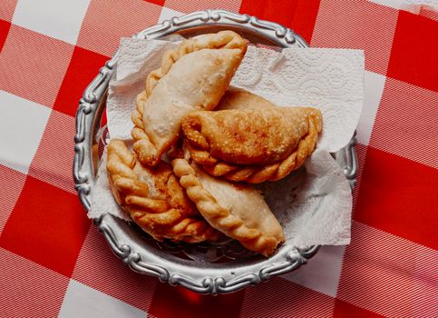 Basket of fried empanadas on a red and white checkered tablecloth, showcasing Argentine cuisine.