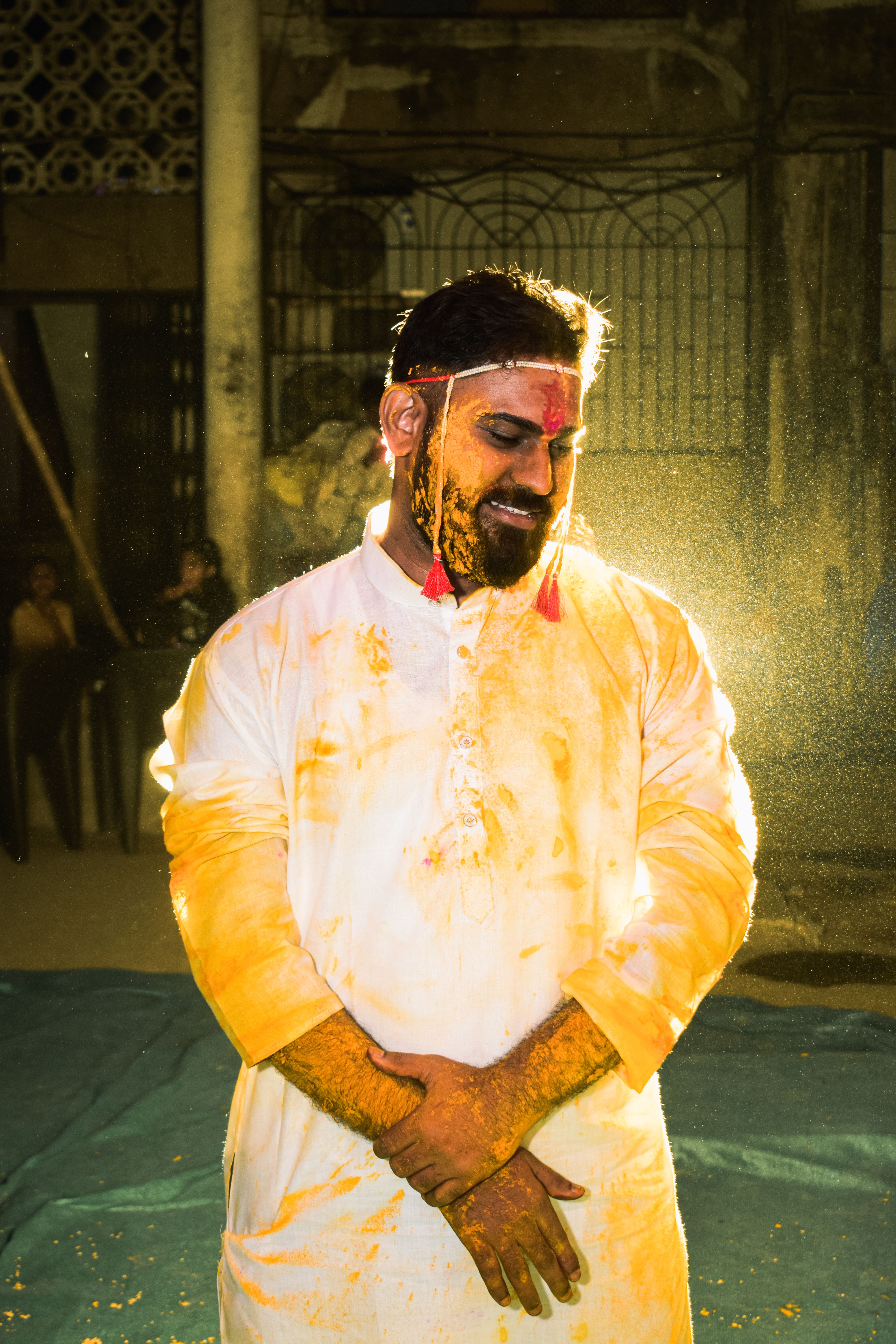 A South Asian man enjoying a vibrant cultural celebration in India, smeared with bright colors and joyful expressions.